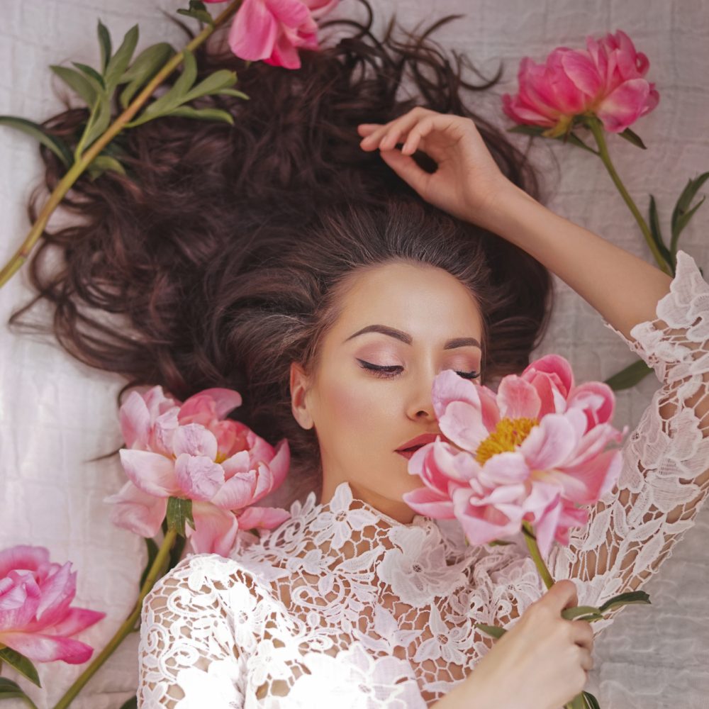 Stylish fashion photo of beautiful young woman lies among peonies. Holidays and Events. Valentine's Day. Spring blossom. Summer season