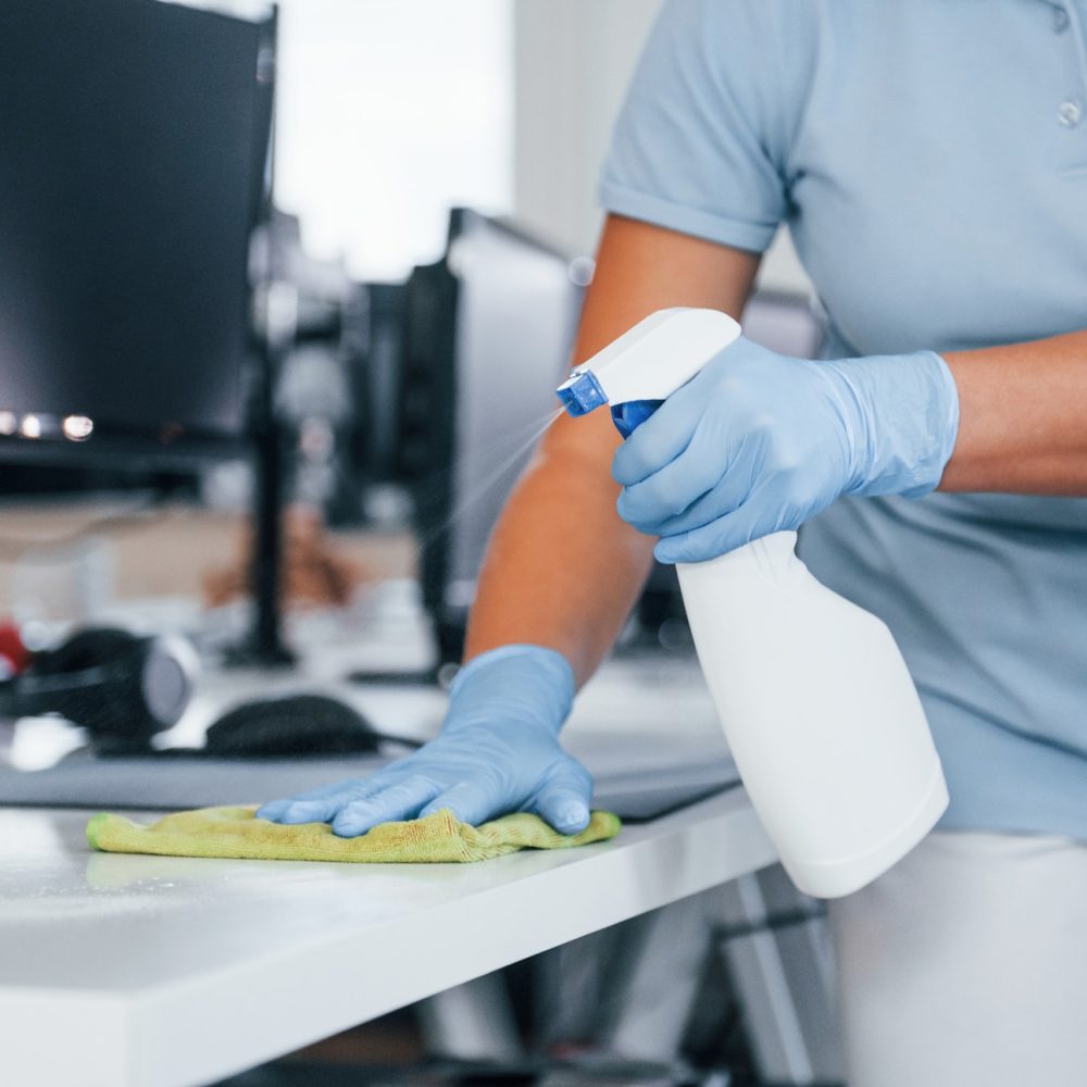 Close up view of woman in protective gloves that cleaning tables in the office