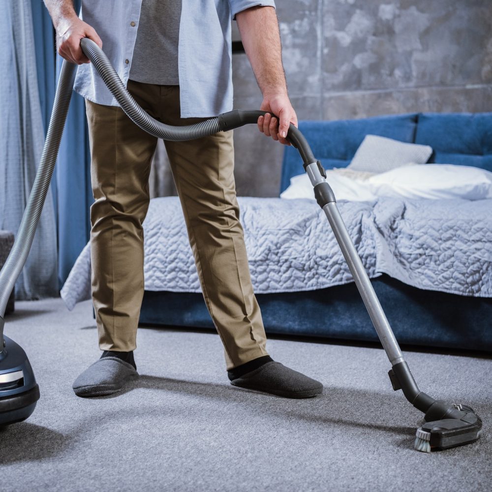Partial view of man with vacuum cleaner cleaning carpet in bedroom
